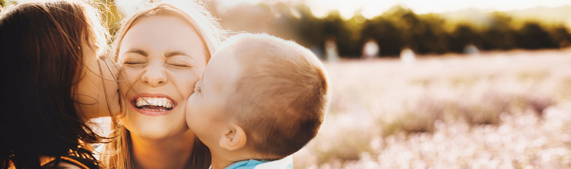 Caucasian mother kissed by her children posing In a Lavender field smiling in a sunny summer day